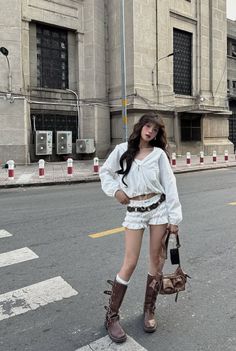 Woman in white top and shorts with brown boots standing on a street