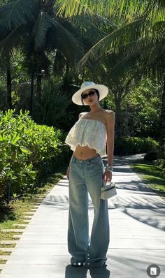 Woman in a white crop top, wide leg jeans, and a hat outdoors