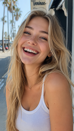 Blonde woman with freckles smiling outdoors in a white tank top