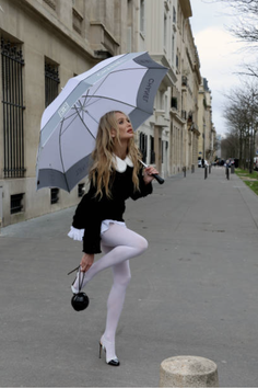 Woman in a black dress and white tights holding an umbrella on a city street