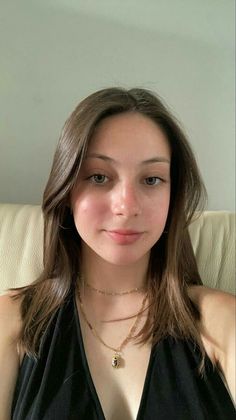 Young woman with long brown hair and gold necklaces wearing a black top indoors