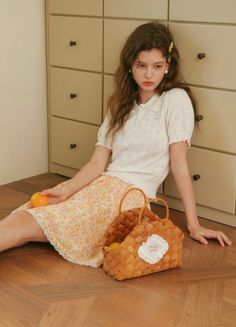 Young woman with long wavy hair sitting on a wooden floor with a basket and an orange