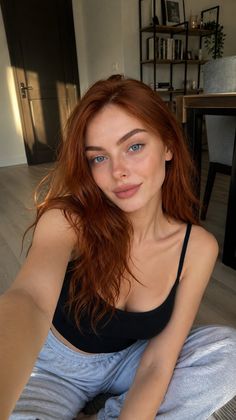 Woman with red hair and blue eyes in a black tank top and grey sweatpants