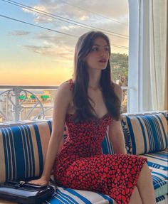 Woman in a red heart-patterned dress sitting on a balcony at sunset