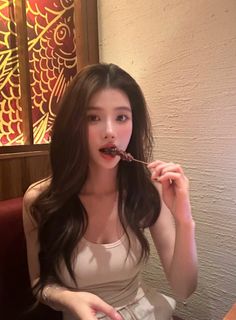 Woman with long dark hair eating a skewer indoors