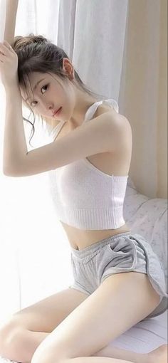 Woman in a white crop top and grey shorts posing indoors