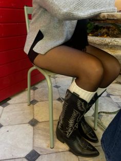 Person wearing cowboy boots, white socks, and tights while sitting on a chair