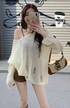Woman in a distressed sweater and shorts taking a selfie on a street