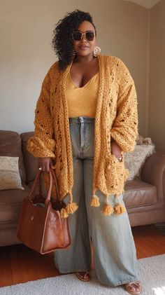 Woman in a chunky knit cardigan, wide leg jeans, and sunglasses holding a brown bag