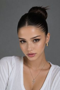 Woman with dark hair in a bun, wearing a white shirt and cross necklace