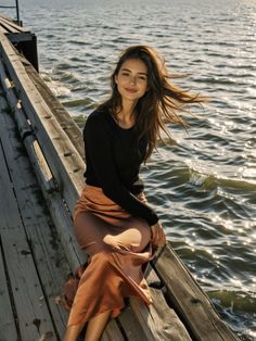 Woman with long hair sitting on a wooden pier by the water at golden hour