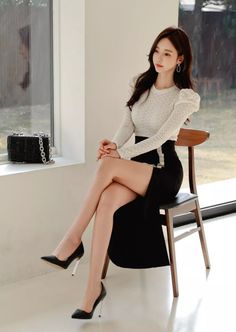 Woman with long hair sitting on a chair in a black skirt and high heels