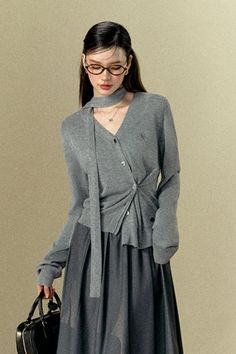 Woman in a gray cardigan and midi skirt with glasses and a black handbag