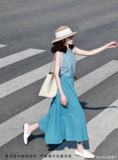 Woman in a blue dress and straw hat crossing a street on a sunny day