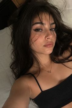 Woman with long dark hair and eyeliner wearing a black top and gold necklace