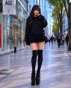Woman in a black hoodie and mini skirt with thigh-high socks on a city street