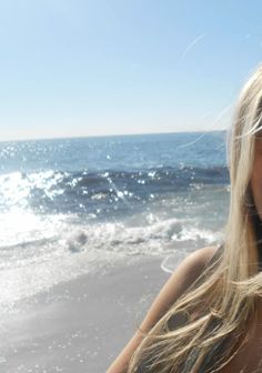 Blonde hair and shoulder with a sparkling ocean and beach in the background