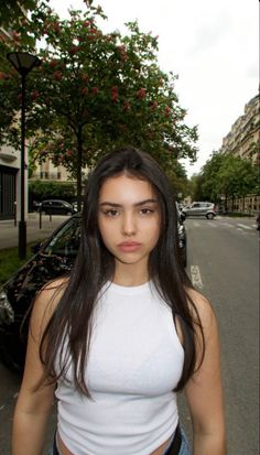 Woman with long dark hair wearing a white tank top on a street