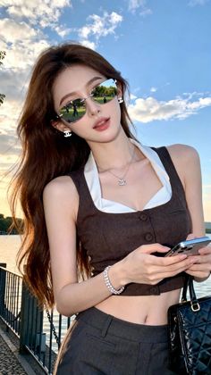 Woman in a crop top and sunglasses holding a phone outdoors at golden hour