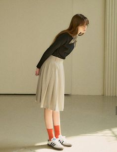 Woman in a black top and pleated skirt with orange socks and sneakers