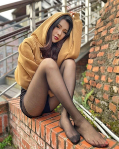 Woman in a brown hoodie and black tights sitting on a brick wall