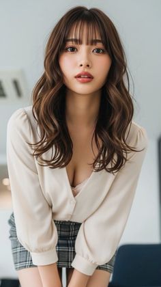 Woman with long wavy hair and bangs wearing a blouse and plaid skirt