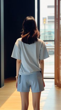 Woman in a light blue t-shirt and shorts standing indoors with backlight