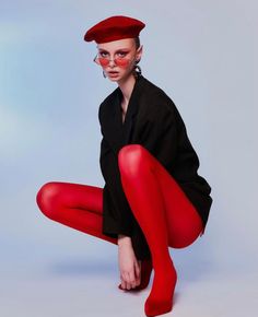 Person in a red beret, red tights, and black blazer squatting in a studio