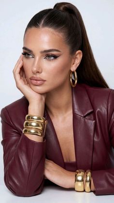 Woman with a high ponytail and gold jewelry wearing a burgundy jacket