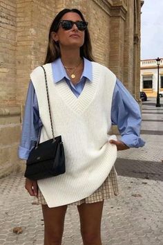 Woman in a white sweater vest and blue shirt with a plaid skirt and sunglasses