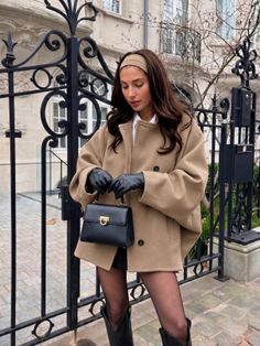 Woman in a tan coat and black gloves holding a handbag outdoors