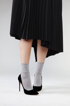 Lower body of a person wearing a black pleated skirt, high heels, and sheer socks