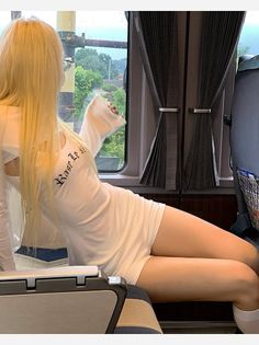 Woman with long blonde hair in a white dress on a train looking out the window