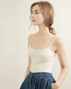 Woman in a white tank top and denim skirt with hair in a ponytail