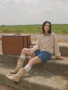 Woman in denim shorts and cowboy boots sitting on concrete steps with a suitcase