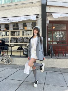 Woman in a gray blazer and white dress posing outside a bakery