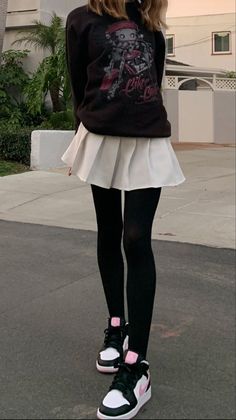 Person in a black sweatshirt, white pleated skirt, and black tights outdoors