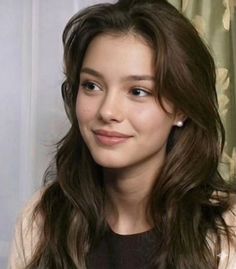 Woman with long brown hair and pearl earrings smiling indoors