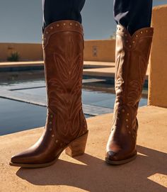 Pair of brown leather cowboy boots with embroidered design and studs outdoors