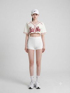 Woman in a white cropped baseball jersey and shorts with a white cap