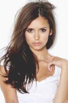 Woman with long brown hair wearing a white t-shirt, looking directly at the camera