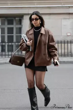 Woman in a brown jacket, black mini skirt, and boots walking on a street