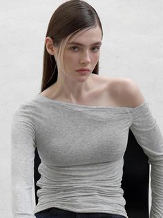 Woman with long hair wearing a grey off-shoulder top indoors