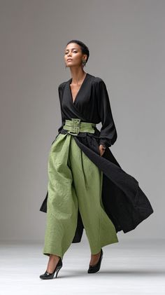Woman in a black top and green wide-leg pants with a matching belt in a studio