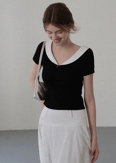 Woman in a black top with a white collar and a white skirt, carrying a shoulder bag