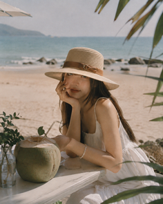 Woman in a straw hat and white dress on a beach with a coconut drink