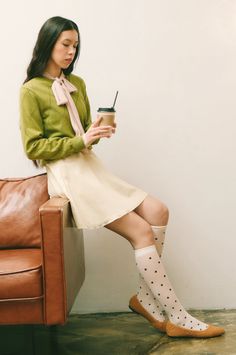 Woman in a green cardigan and polka dot socks holding a coffee cup