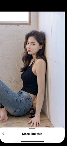 Woman with long wavy hair in a black tank top and blue jeans sitting indoors
