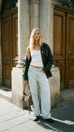 Blonde woman in a leather jacket and light wash jeans standing outdoors