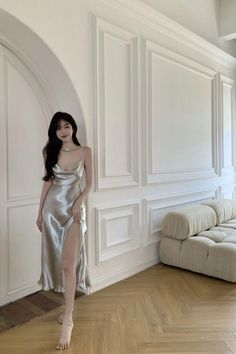 Woman in a silver cowl neck dress with a high slit standing barefoot indoors